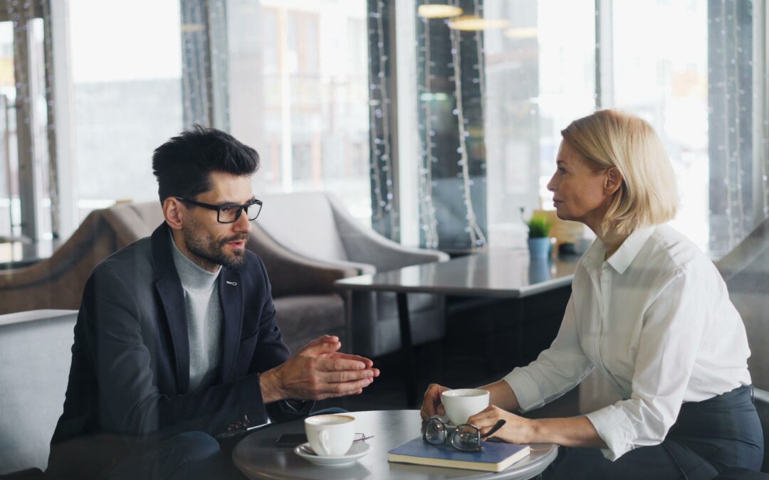 Man and woman having a serious conversation over coffee in a professional office setting.